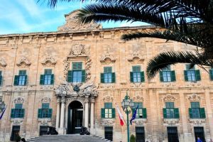 A tall and wide building with green open windowsills and a palm on the side of the image