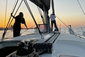 A small white sailboat and two silhouettes standing in front of it, with a sunset at the back