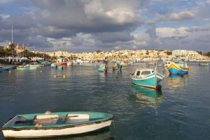 Blue and yellow boats floating on the sea surface at a rural area with clouds in the sky. The sun is peeking through