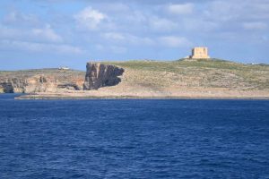 A foreground of sea and background of an island with a white tower on top