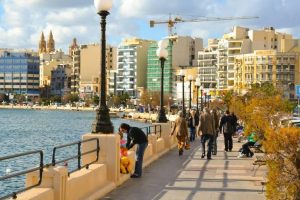 Sliema's Promenade on a sunny day, with a view of the cityscape and a corner of the sea.