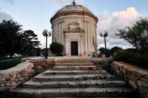 Small decadent tan colored chapel perched on a stone platform atop a short stone staircase.